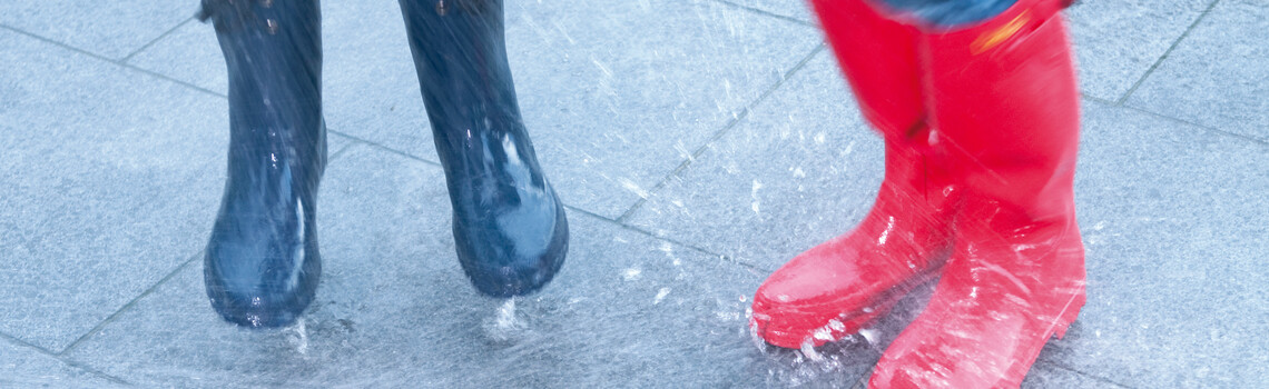 Beine im Regen mit Gummistiefel die im Regen auf einer Terrasse stehen und springen | © Gutjahr Systemtechnik