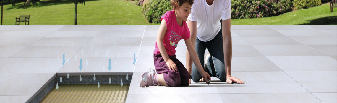 Vater mit Mädchen sitzen auf deinem Terrassenbelag im Untergrund eine Drainage | © Gutjahr Systemtechnik