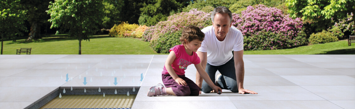Vater mit Mädchen sitzen auf deinem Terrassenbelag im Untergrund eine Drainage | © Gutjahr Systemtechnik