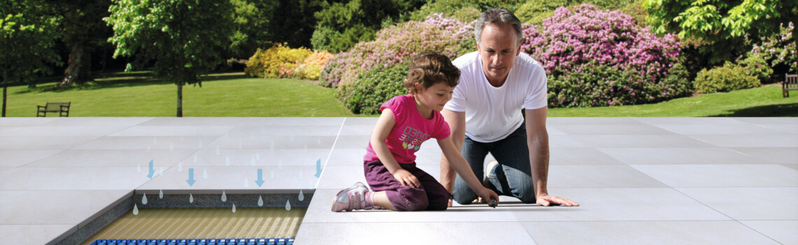 Vater mit Mädchen sitzen auf deinem Terrassenbelag im Untergrund eine Drainage | © Gutjahr Systemtechnik