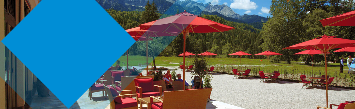 Terrasse mit roten Schirmen und einer Berglandschaft im Hintergrund