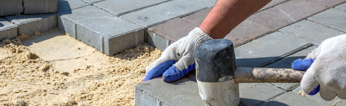 Handwerker der ein Betonwerkstein fest klopft